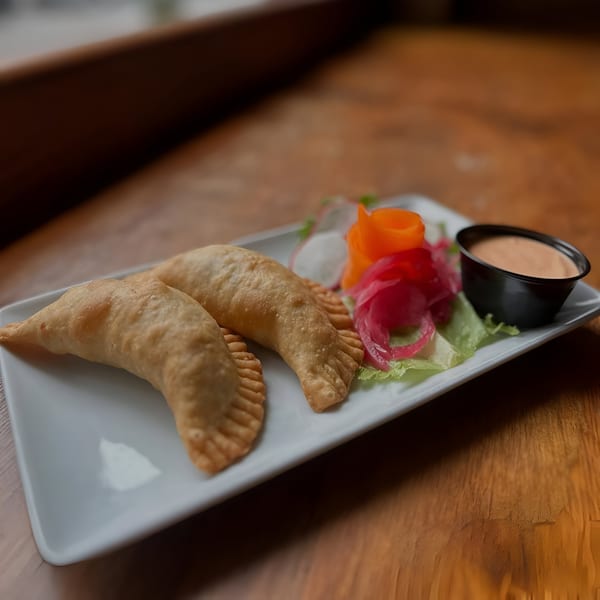 Two golden-brown empanadas with a side of pickled vegetables and dipping sauce on a white plate.