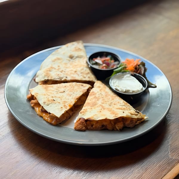 Four quesadilla wedges with melted cheese, salsa, and sour cream on a gray plate.