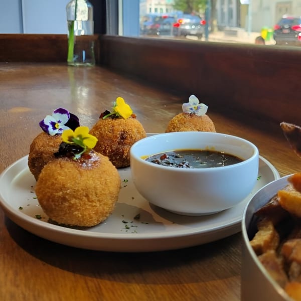 Crispy arancini balls garnished with edible flowers and a side of dark dipping sauce.
