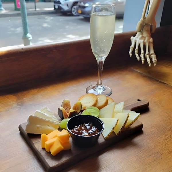A cheese board with various cheeses, figs, grapes, crackers, and jam, with a champagne flute.