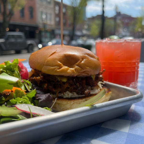 Pulled pork sandwich with a side salad and a red drink on a blue checkered tablecloth.