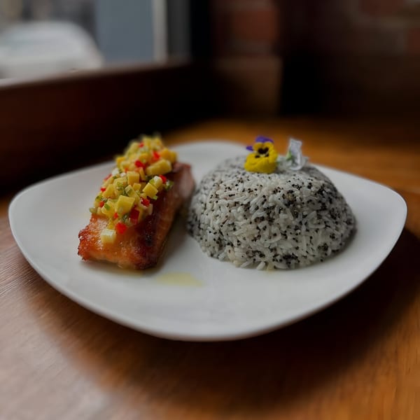 Grilled salmon with mango salsa and a side of black and white rice, garnished with a flower.